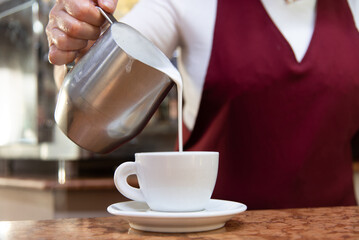 barista pours milk to make a cappuccino