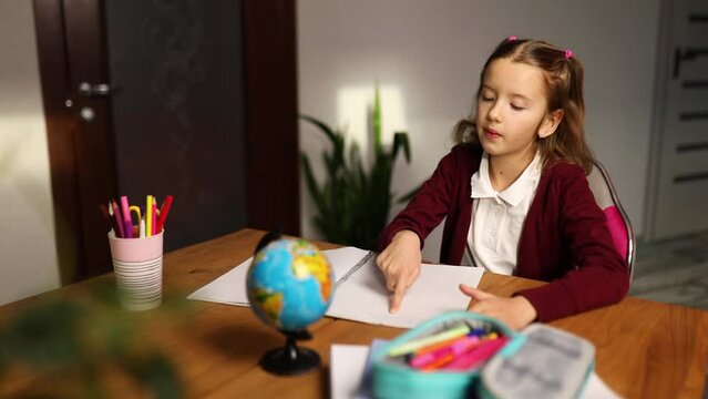 Bored schoolgirl sit at desk doing homework reading, homeschooling. Small junior girl tired of distant learning get remote elementary education and preparing for exams.