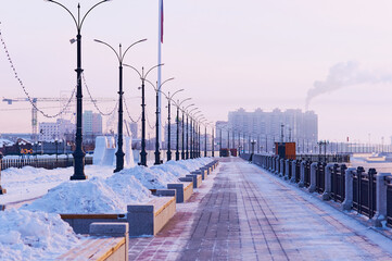 Promenade of the city of Blagoveshchensk on a winter morning after clearing the snow. Snowdrifts on flowerbeds and benches.
