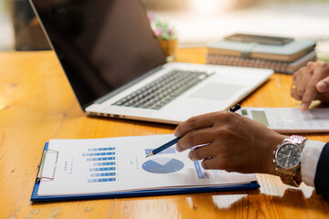 Businessman hand holding pen pointing to marketing graph and working on laptop computer and a calculator to calculate work concepts online