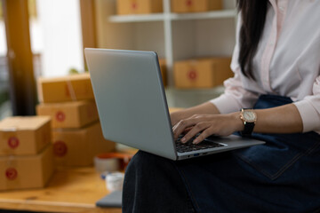 Naklejka premium Start a small business SME entrepreneur or independent young Asian woman using laptop with box online marketing and delivery, SME work-at-home concept.