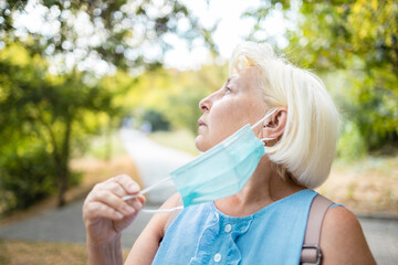 50s 60s caucasian blond hair woman takes off her mask outdoors. Coronavirus is over. Healthcare...