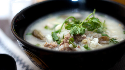 Pork boiled rice with shiitake mushrooms on a black bowl with a spoon on the table.