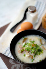 Pork boiled rice with shiitake mushrooms on a black bowl with a spoon on the table.
