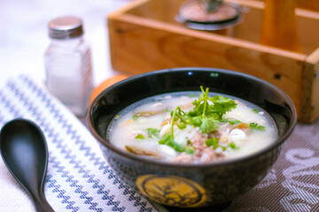 Pork boiled rice with shiitake mushrooms on a black bowl with a spoon on the table.
