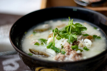Pork boiled rice with shiitake mushrooms on a black bowl with a spoon on the table.