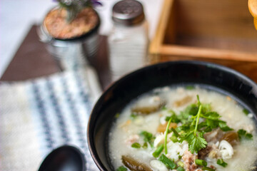 Pork boiled rice with shiitake mushrooms on a black bowl with a spoon on the table.