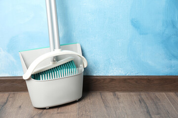 Plastic broom with dustpan near light blue wall indoors. Space for text