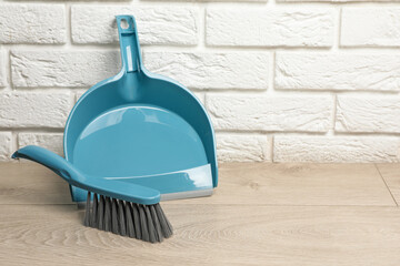 Plastic whisk broom with dustpan near white brick wall indoors. Space for text