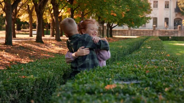 Happy little girl running to hug her brother outoodrs in park in autumn