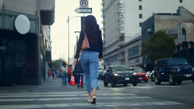 Unrecognized woman walking on crossroad big city. Unknown girl crossing road.