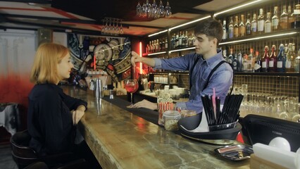 A girl is sitting in a bar with a cocktail in her hands and communicates with the bartender