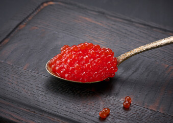 grainy red caviar in a metal spoon on a wooden board