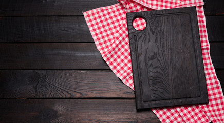 wooden cutting board and folded red and white cotton kitchen napkin on a wooden brown background, top view