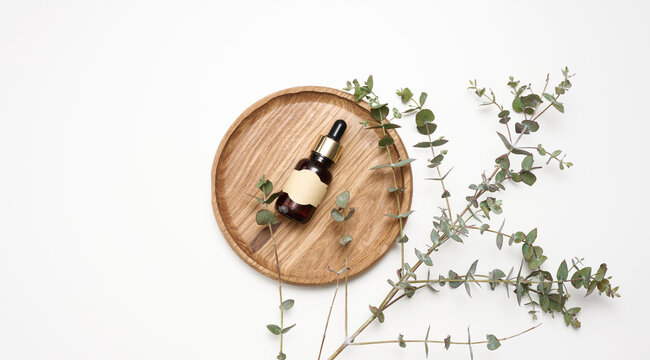 brown glass bottle with a pipette and an empty glued label on a wooden board, next to a branch of eucalyptus
