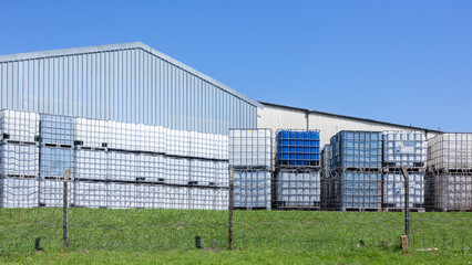 Fototapeta na wymiar Industrial Chemical Holding Tanks With Metal Cage for safe transportation of liquids stacked outdoors in blue sky