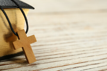 Christian cross and Bible on white wooden table, closeup. Space for text