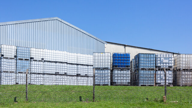 Industrial Chemical Holding Tanks With Metal Cage for safe transportation of liquids stacked outdoors in blue sky