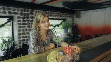 A girl is sitting in a bar with a glass of wine in her hands and communicates with the bartender