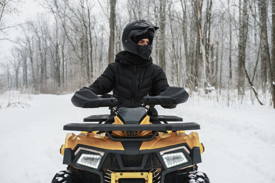 Portrait of a man on an ATV quad bike in winter background. A quadricycle rider in snowy forest, outdoor winter activities