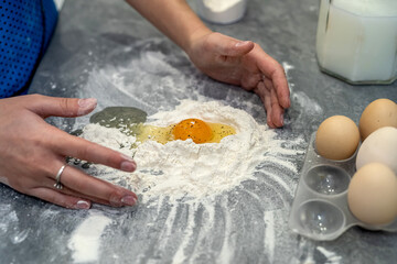  woman is fighting in the kitchen breaking eggs into flour and kneading dough into dumplings.