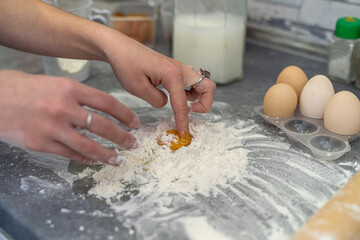 Obraz na płótnie Canvas Beautiful young female hands break eggs into flour to knead a beautiful dough.