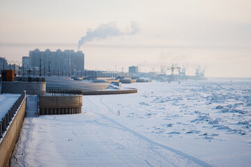 Snow-covered ice of the Amur River on a winter morning. Cranes of the river port in the background.