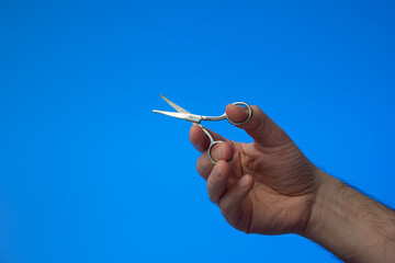 Small all metal scissor held in use by Caucasian male hand. Close up studio shot, isolated on blue background