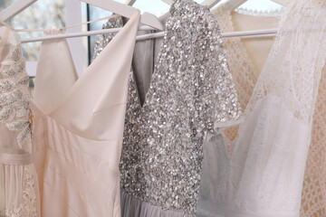 Hangers with different beautiful dresses in atelier, closeup