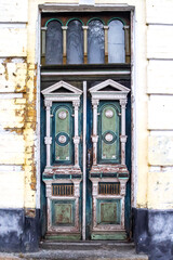 Fototapeta na wymiar Old wooden painted door. Elegant old double-leaf door in an abandoned building in Kiev, Ukraine. An old wooden doorway in the wall of an old stone house. Wooden door with rich carvings.