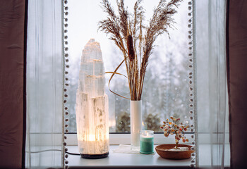 Rough big selenite crystal tower pole lamp illuminated on home window sill, spiritual home decor...