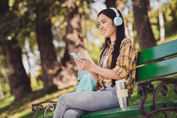 Photo of charming pretty young woman dressed plaid shirt sitting bench listening music player smiling outside countryside nature