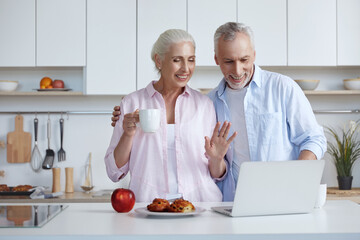 Fototapeta na wymiar Senior couple have video call on laptop at kitchen