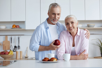 Fototapeta na wymiar Man hugging wife and holding apple at home kitchen