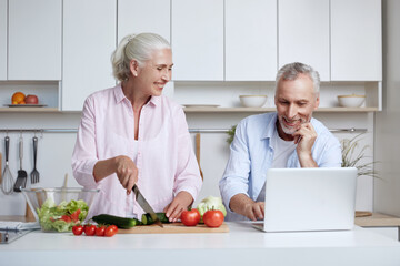 Man use laptop while wife cut cucumber for salad