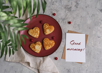 Pancakes in the shape of a heart and postcard with text Good morning. Breakfast for Valentine's Day