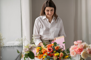 people, gardening and floral design concept - happy smiling woman or floral artist wrapping flowers to craft paper at home