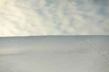Fototapeta na wymiar Snowy slope against sky. Avalanche of snow on mountain ridge. Winter weather.