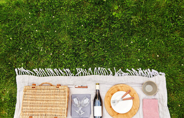 leisure, food and drinks concept - close up of basket, crockery and wine bottle on picnic blanket