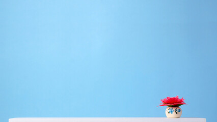 Miniature flower in a ceramic vase on a shelf. Minimal blue background.