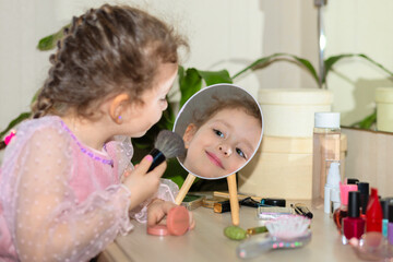 Obraz na płótnie Canvas Happy little cute girl playing with her mother's cosmetic, selfcare, beauty procedure Treatment, makeup, visage, powdering face in front of mirror at home.