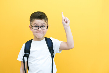 eureka, handsome little boy in glasses is surprised, inspired, i have an idea, raise your index finger up, copy space, isolated on yellow background.