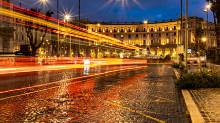 Fototapeta na wymiar Cars light trails in the evening square in Rome right after the rain. Night traffic routes. Motion blur. Cityscape.