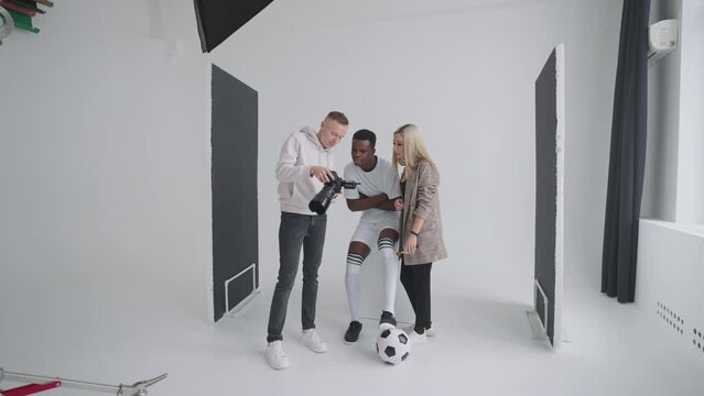 A photographer, a football player, a model and a director look at photos from a photo shoot for the cover of an advertising magazine on a camera