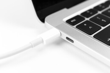 Charging battery laptop. Modern USB C port for fast charge. White cable plugged in laptop close-up view photo