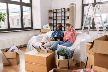 moving, people and real estate concept - happy smiling women with tablet pc computer and boxes making plans at new home