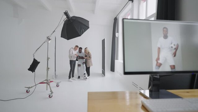 Monitor with an advertising cover of the picture On the background a photographer, a football player, a model and a director look at photos from a photo shoot for the cover on a camera