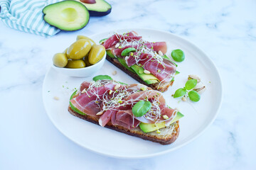 Whole grain bread sandwiches with slices of avocado, prosciutto or jamon, germinated seeds and herbs. Clean eating, healthy breakfast. Top view.