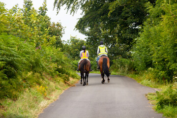 Couple riding along country roads in rural Wales, wearing bright safety gear to be seen and keep themselves and other road users safe.