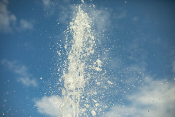 The fountain jet against the background of the sky. Water drops on the background of clouds and blue sky.